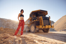 Young Woman In Red Pants And Black Top Is Standing In The Quarry Against Haul Truck