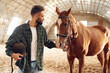 Positive emotions. Front view. Young man with a horse is in the hangar