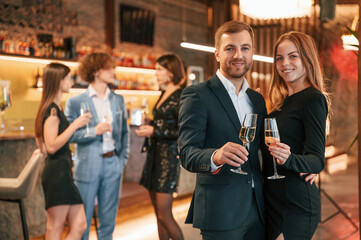 Wall Mural - Man with his woman is standing and smiling. Group of people in beautiful elegant clothes are celebrating New Year indoors together