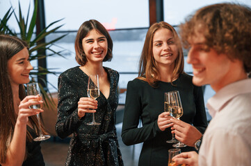 Wall Mural - Against big panoramic windows. Group of people in beautiful elegant clothes are celebrating New Year indoors together