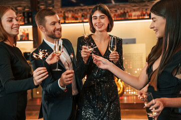 Wall Mural - Champagne and sparklers. Group of people in beautiful elegant clothes are celebrating New Year indoors together