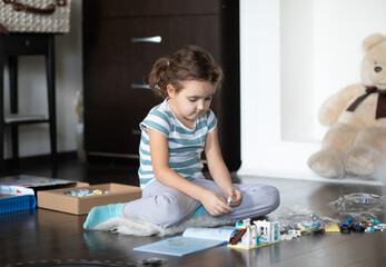 Little cute girl playing with colorful toys construction blocks at home.