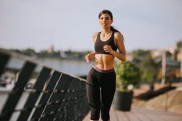 Wall Mural - Active young beautiful woman running on the promenade along the riverside