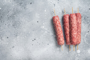 Raw kofta or lula kebabs skewers on butcher board. Gray background. Top view. Copy space