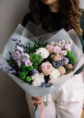 Wall Mural - Very nice young woman holding beautiful bouquet of fresh tender roses, carnations, matthiola, hyacinths, pistachio flowers in green, white and purple colors, cropped photo, bouquet close up