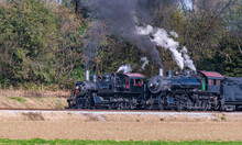 A View Of Two Steam Engines, Blowing Smoke And Steam Warming Up Next To Each Other On A Sunny Day