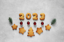 Cookies In The Form Of Numbers 2023 In The Center On The Concrete Background Decorated With Pine Twig And Christmas Toys. Concept New Year, Top View