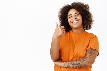 Portrait of smiling african american woman shows thumbs up, nod in approval, recommends, likes smth good, standing over white background