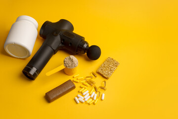 Wall Mural - Therapeutic percussive massage gun, fit meal, pills, sport energy bar, protein on yellow background - concept of modern sport activity and diet, health lifestyle routine, wellness, healthcare