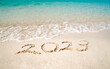 Top view of 2023 numbers written on the sand of coastline with frothy waves. 2023 new year concept.