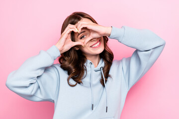 Sticker - Photo of positive funny young lady wear grey hoodie looking showing arms heart isolated pink color background