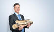 Confident businessman in a dark suit and tie holds firewood for heating the house on a light blue background