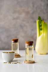 Two bottles of essential fennel oil with fennel seeds and fresh bulb on white and grey background