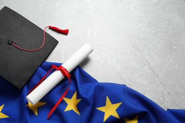 Wall Mural - Black graduation cap, diploma and flag of European Union on light grey marble table, above view. Space for text