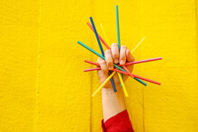 Hand Of Woman Holding Colored Pencils In Front Of Yellow Wall