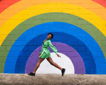 Woman Jumping In Front Of Rainbow Flag Painted On Wall