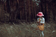 Little stylish girl in a pink hat walks in a flowering summer meadow