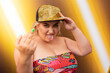 © VISTA by Westend61 - Young woman wearing cap sticking out tongue against glowing yellow light