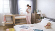 © PRPicturesProduction - asian mother holding her baby upright is coaxing by patting gently on the back in a bright bedroom with scattered infant clothing.