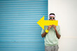 © VISTA by Westend61 - Man holding yellow arrow sign in front of lips by blue shutter