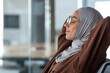 Closeup dreamy woman in hijab and glasses eyes closed with hands behind her head sitting on a chair in the office, business woman successfully completed her work resting in the day and dreaming.