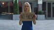 © kinomaster - Young woman stands with a cardboard poster NO RACISM in a public place outdoor. A protesting political activist at a protest. No racism but tolerance and political correctness in society