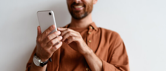Partial view of blurred man using mobile phone near wall, banner crop 