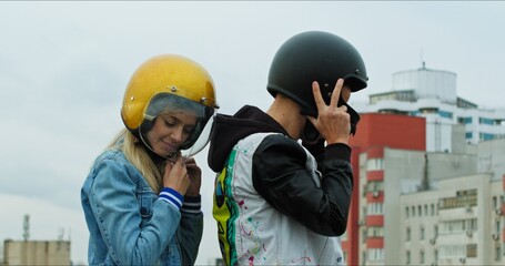 Wall Mural - A young stylish couple of bikers sit on a bike standing in a public city parking. The guy and the girl put on motorcycle helmets. Love and safety