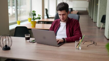 Wall Mural - young freelancer man working with laptop at bright spacious coworking alone. creative designer at wo