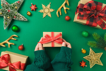 Wall Mural - Merry Christmas concept with gift box, woman hands and decorations on green background. Top view, flat lay