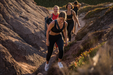 Wall Mural - Full length view of the brunette women going through the grassy hill with yoga mats