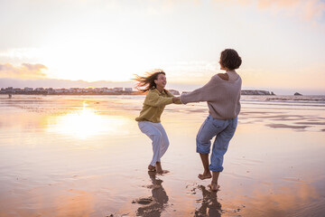 Barefoot girls holding hands and spinning at the beach