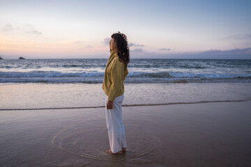 Wall Mural - Hipster girl standing barefoot at the sandy beach and looking at the sunset