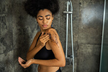 Curly African American Woman In Crop Top Massaging Shoulder With Coffee Scrub In Shower.