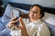 Overweight woman laying on the bed and looking at the screen of her mobile phone
