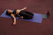 Above view of flexible girl practicing yoga pose on yoga mat. Young slim brunette female lying barefoot on legs with hands aside and closed eyes. Concept of new age reality.