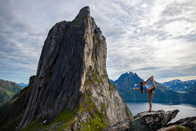 backpacker girl stretches (yoga - dancer position) on the rocks overlooking the famous segla mountain in norway, senja island; hesten trail head, the famous norwegian fjords with mighty mountains