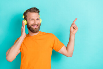 Wall Mural - Photo of cheerful positive optimistic man dressed orange t-shirt indicating empty space touch headphones isolated on teal color background