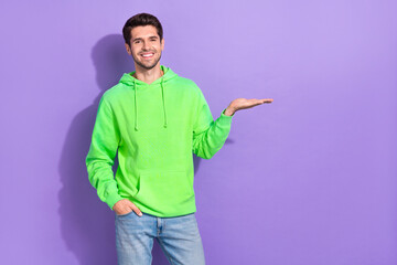 Sticker - Photo of satisfied guy with brunet hairdo dressed green hoodie hand pocket demonstrating empty space isolated on purple color background