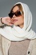 blonde woman in headscarf and stylish sunglasses posing isolated on grey.