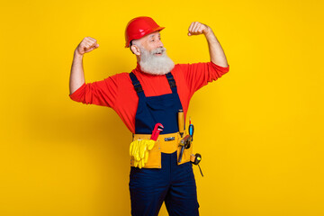 Wall Mural - Photo of strong powerful old guy dressed uniform overall red hardhat rising hands showing biceps empty space isolated yellow color background