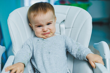 A small child is sitting on a high chair and crying. Baby chair for feeding. A small child is sitting. Children's emotions