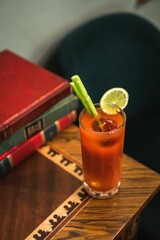 Canvas Print - Bloody mary decorated with parsley sprig and lime on an old wooden table and with old colored books