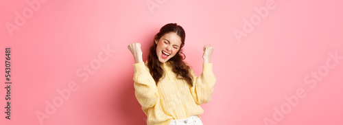 Fototapete Girl screams with joy and fist pump, say yes, achieve goal or success, celebrating achievement, triumphing and winning, standing over pink background