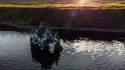 Hvitserkur basalt stack rock which looks like an elephant or dragon on the flowing water with view of cliff, waterfall, field and sunlight