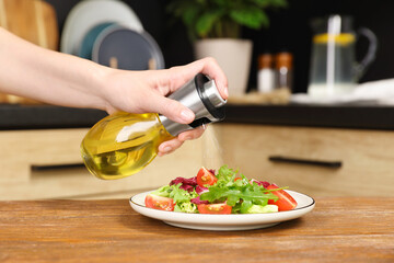 Woman spraying cooking oil onto salad on wooden table in kitchen, closeup