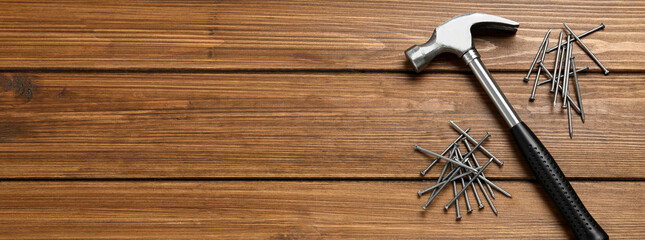 Hammer and metal nails on wooden table, flat lay with space for text. Banner design