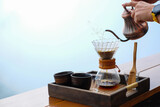 Fototapeta Sport - Pouring water on a drip coffee set with a steel kettle and glasses on the wooden table with mountain in the natural mist background..