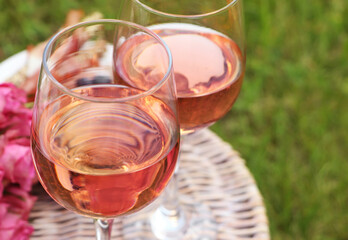 Canvas Print - Glasses of delicious rose wine and flowers on picnic basket outdoors, closeup