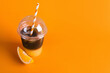 Tasty refreshing drink with coffee and orange juice in plastic cup on bright color background, space for text